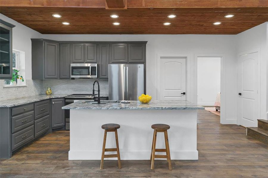Kitchen featuring appliances with stainless steel finishes, dark wood-type flooring, an island with sink, and backsplash
