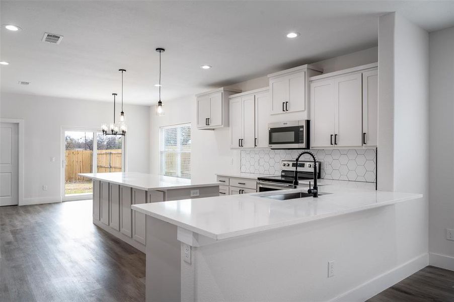 Kitchen with a center island, backsplash, dark hardwood / wood-style flooring, appliances with stainless steel finishes, and pendant lighting