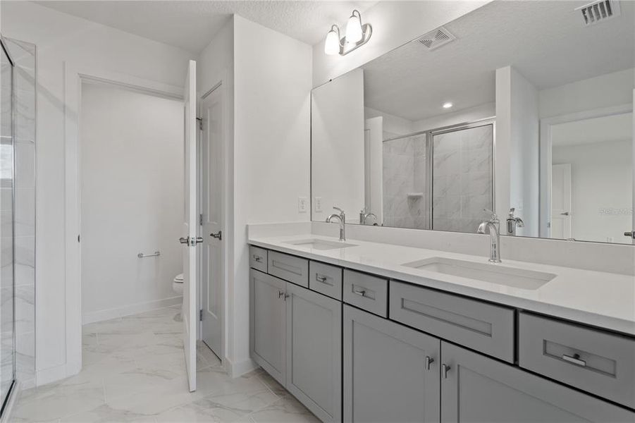 Spacious primary bathroom with two sinks, a shower and private water closet.