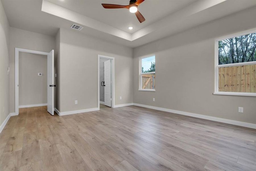 Unfurnished bedroom with ceiling fan, a raised ceiling, and light hardwood / wood-style flooring