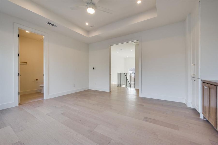 Empty room with a raised ceiling, light wood-type flooring, and ceiling fan