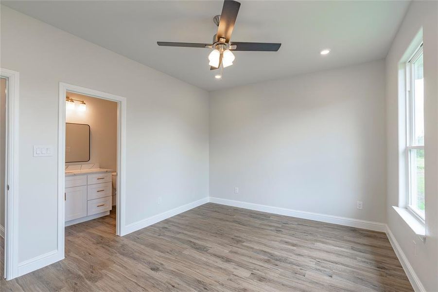 Unfurnished bedroom featuring ensuite bathroom, ceiling fan, and light hardwood / wood-style floors