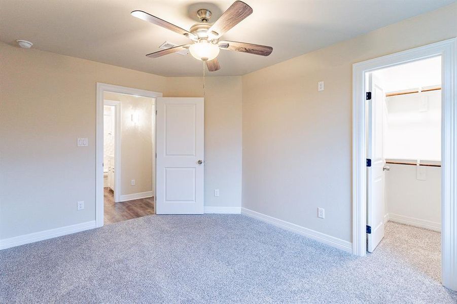 Unfurnished bedroom featuring light colored carpet, ceiling fan, a walk in closet, and a closet