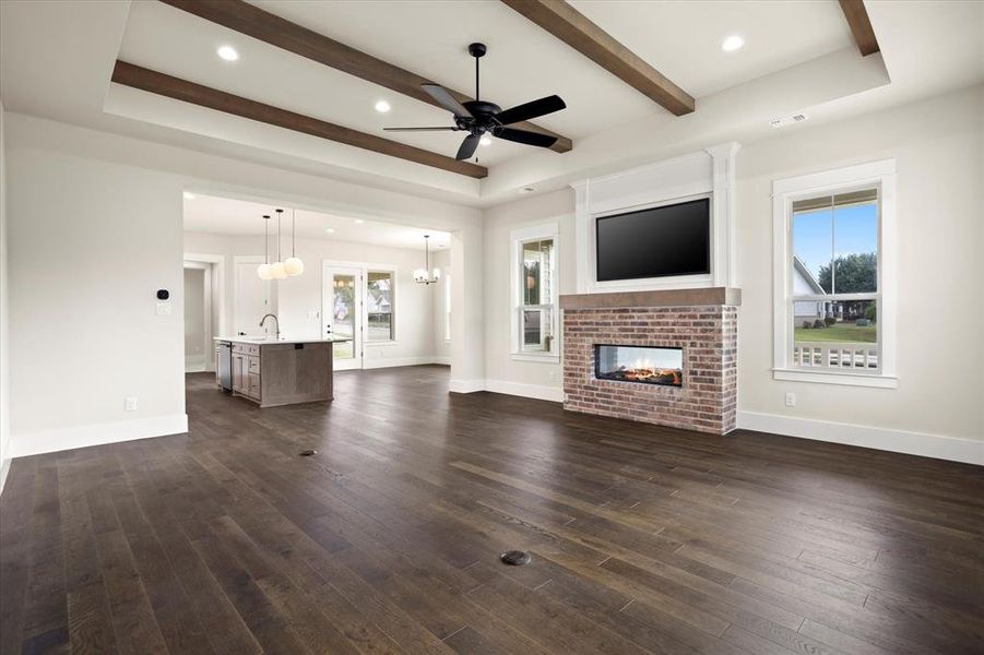 Unfurnished living room featuring a brick fireplace, ceiling fan with notable chandelier, sink, dark hardwood / wood-style floors, and beam ceiling