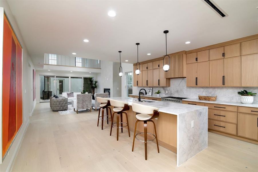 Kitchen with a spacious island, a kitchen breakfast bar, light stone counters, sink, and light hardwood / wood-style floors