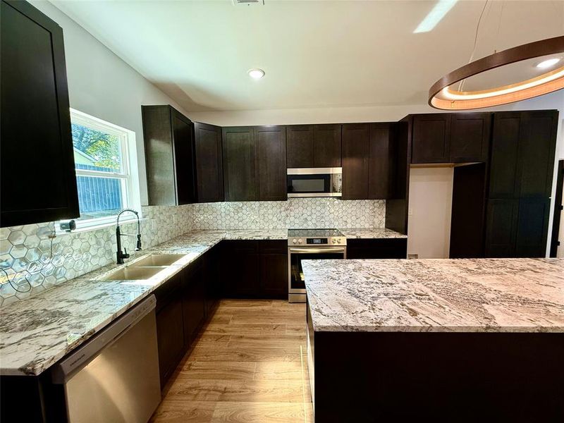 Kitchen featuring tasteful backsplash, appliances with stainless steel finishes, light stone countertops, light wood-type flooring, and sink