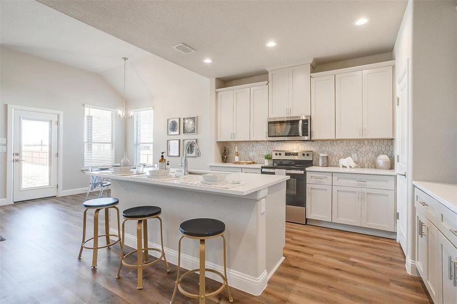 Kitchen with light wood-type flooring, an island with sink, white cabinets, lofted ceiling, and appliances with stainless steel finishes