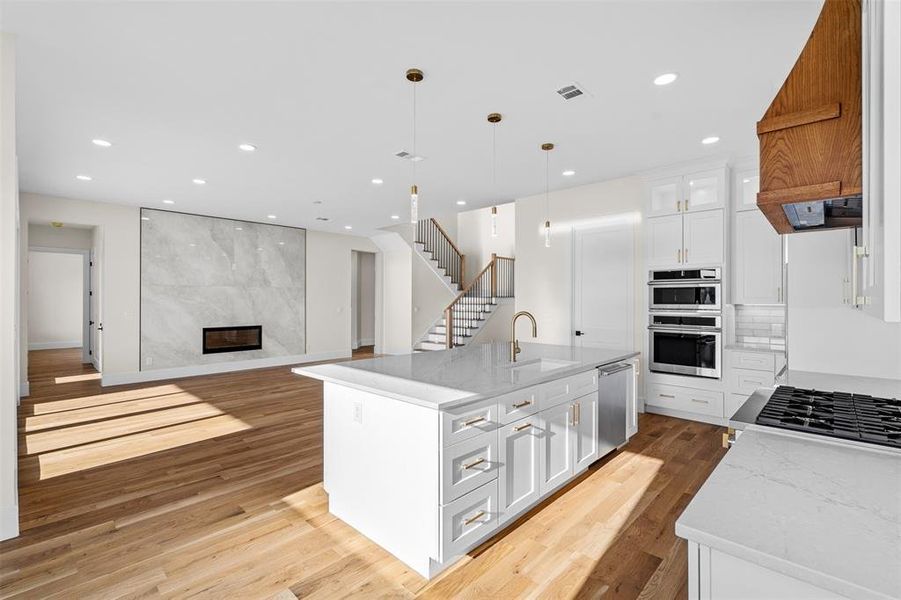 Kitchen featuring white cabinets, an island with sink, hanging light fixtures, sink, and light hardwood / wood-style flooring