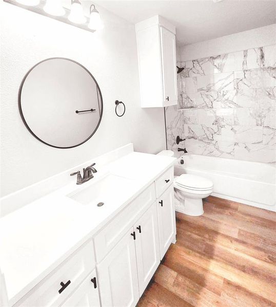 Full bathroom with hardwood / wood-style floors, vanity, tiled shower / bath combo, and toilet