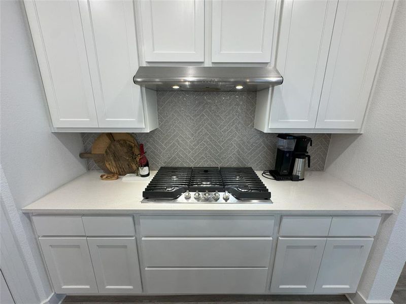 Kitchen with backsplash, wall chimney range hood, black gas cooktop, and white cabinets