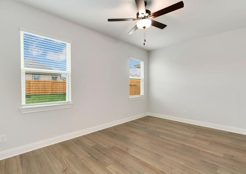 Large master bedroom with windows, tan carpet, and a ceiling fan.