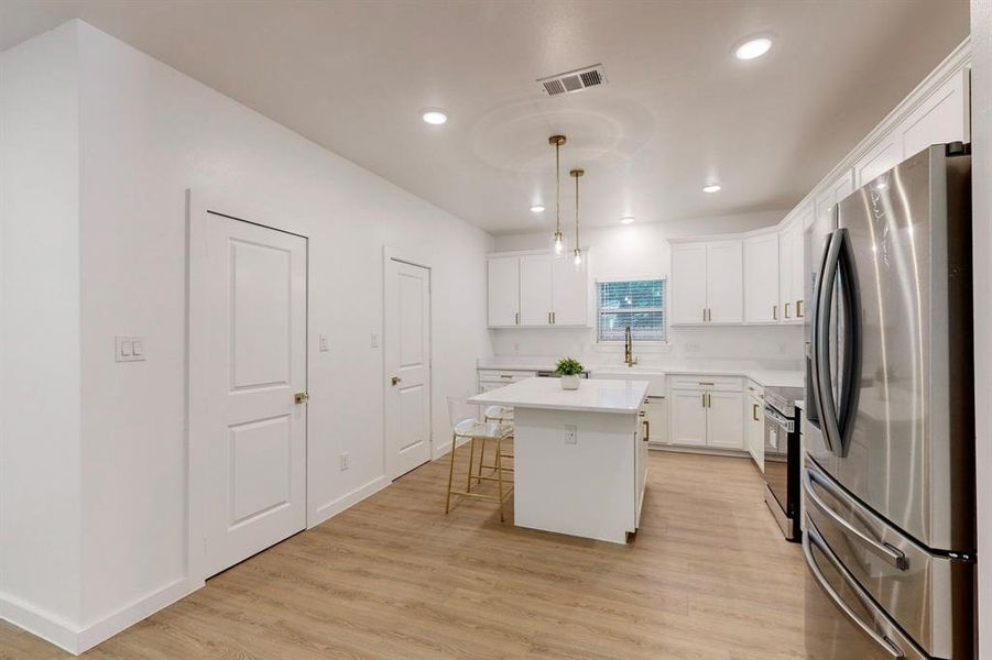 Kitchen with pendant lighting, light hardwood / wood-style floors, stainless steel refrigerator, and a kitchen island