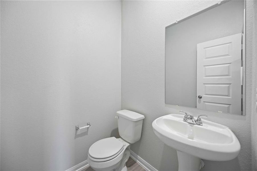 This half bathroom features a stylish pedestal sink, modern hardware, and bright recessed lighting, creating a sleek and inviting space.