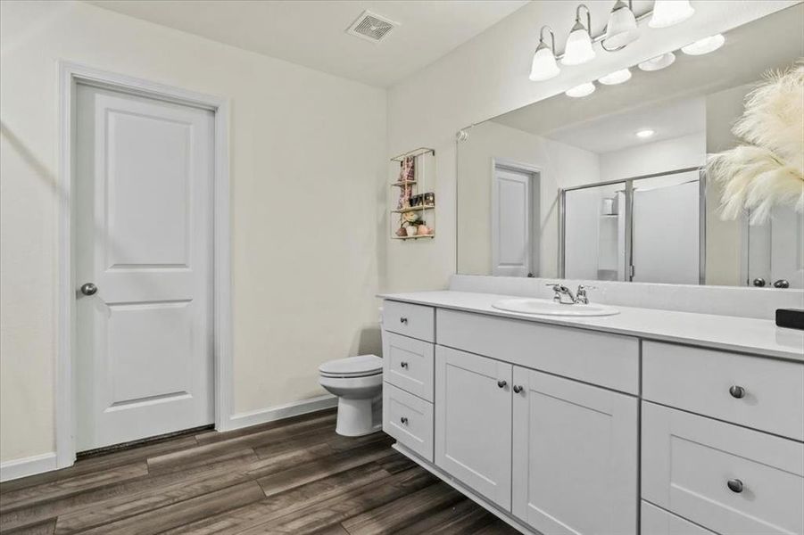 Bathroom featuring vanity, hardwood / wood-style floors, toilet, and a shower with door