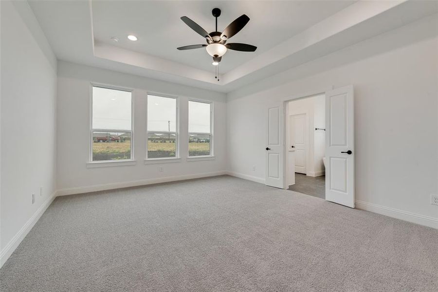 Unfurnished bedroom featuring ceiling fan, light carpet, and a tray ceiling