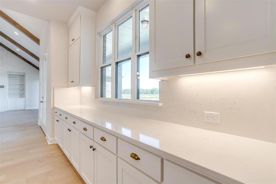 Kitchen with white cabinetry, built in shelves, light hardwood / wood-style floors, light stone countertops, and lofted ceiling with beams