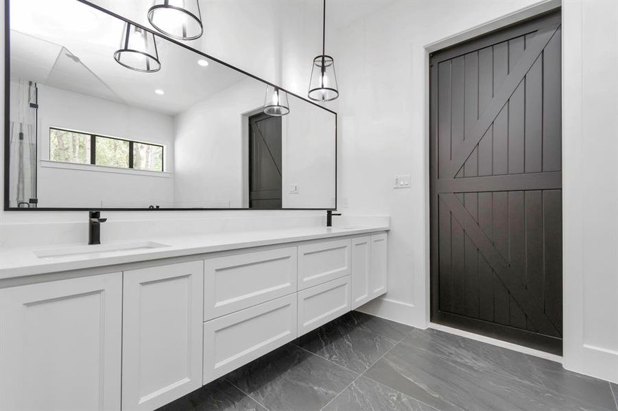 Modern bathroom featuring white cabinetry, dual sinks, large mirror, sleek black fixtures, and a stylish dark door. Natural light from window.