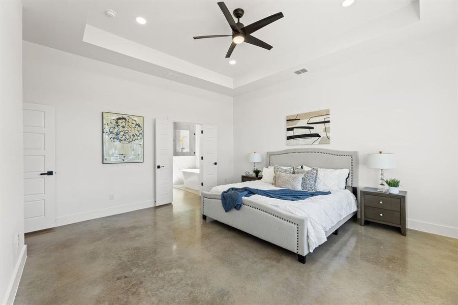 Bedroom featuring ceiling fan, a raised ceiling, concrete floors, and ensuite bath