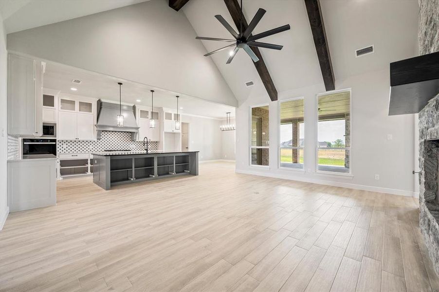 Living room featuring a fireplace, ceiling fan, light wood-type flooring, high vaulted ceiling, and beam ceiling