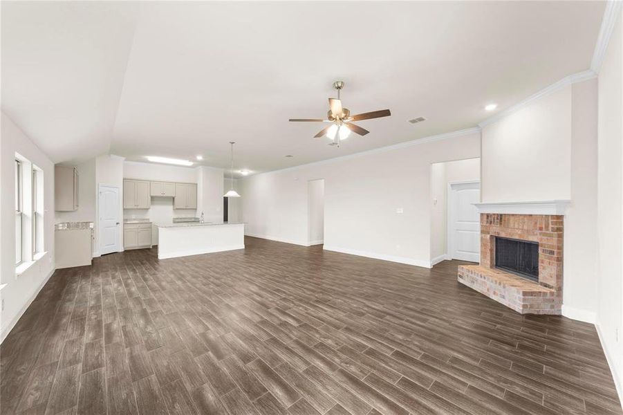 Unfurnished living room featuring a brick fireplace, ornamental molding, dark hardwood / wood-style flooring, and ceiling fan