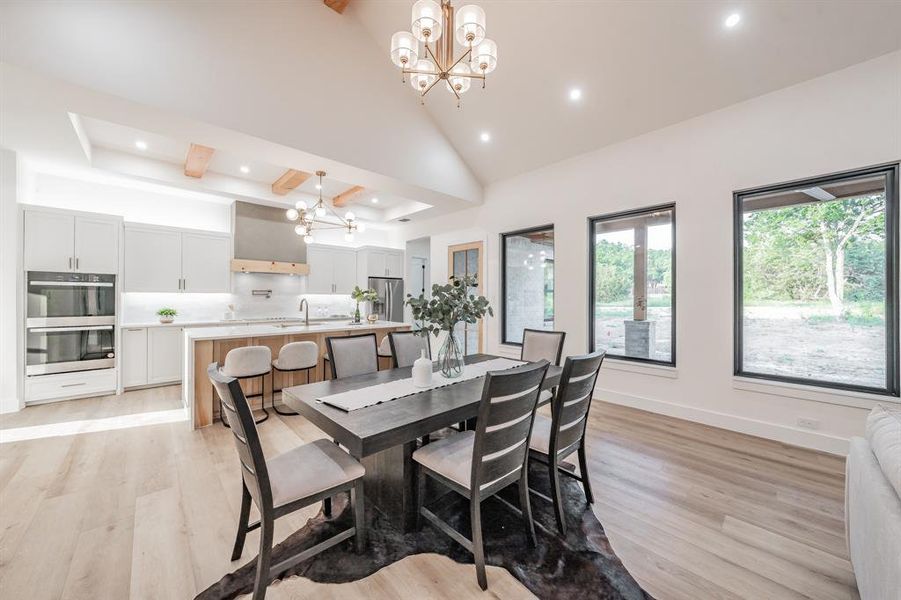 Dining area featuring a notable chandelier, sink, a high ceiling, and light blonde plank, wood-like luxury vinyl floors.