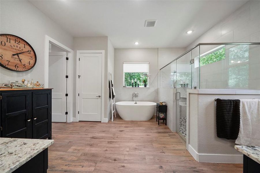 The luxurious primary bathroom features a spacious layout with elegant finishes. Enjoy the freestanding soaking tub and the large walk-in shower with custom tile work and frameless glass, while dual vanities with granite countertops provide ample storage and convenience.