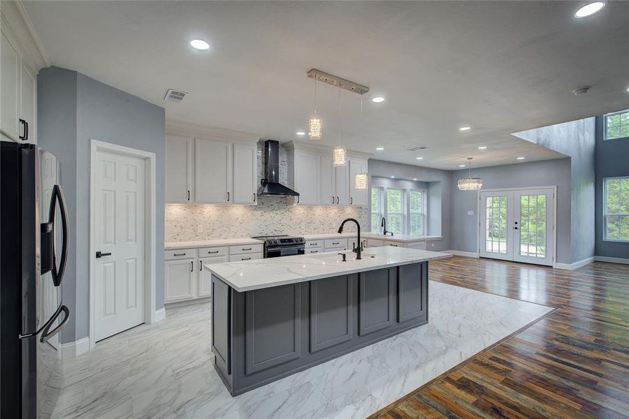 Kitchen featuring stainless steel appliances, a center island with sink, wall chimney range hood, pendant lighting, and light wood-type flooring