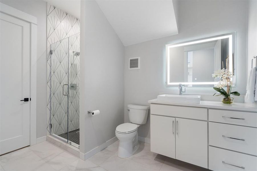 In the guest bath, a modern illuminated mirror adds a touch of elegance, complimenting the convenience of the step-in shower for a refreshing and comfortable experience for all visitors