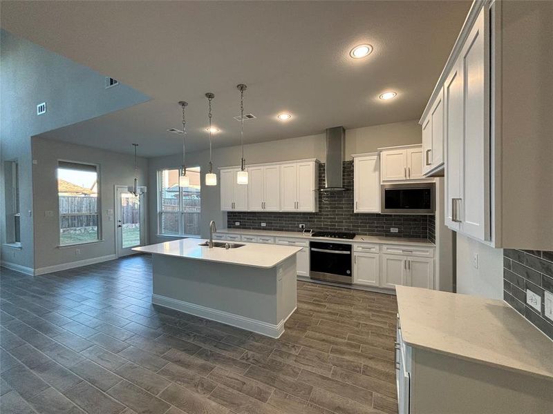 Kitchen featuring wall chimney range hood, sink, appliances with stainless steel finishes, white cabinetry, and decorative light fixtures