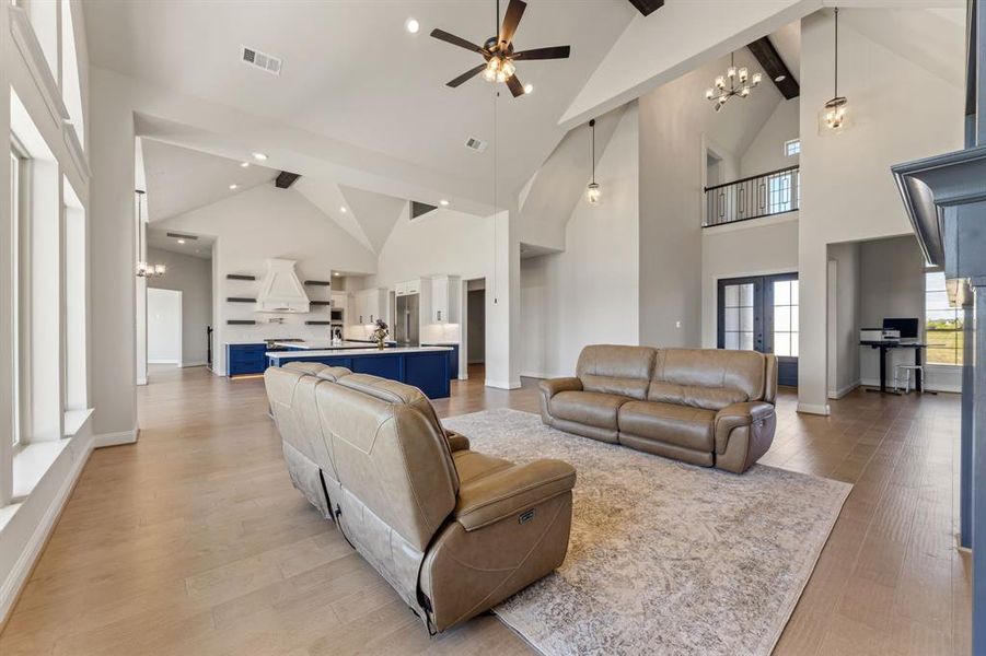 Living room featuring ceiling fan with notable chandelier, light wood-type flooring, beam ceiling, and high vaulted ceiling