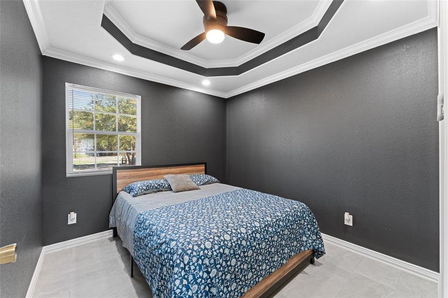 Tiled bedroom with ceiling fan, ornamental molding, and a tray ceiling