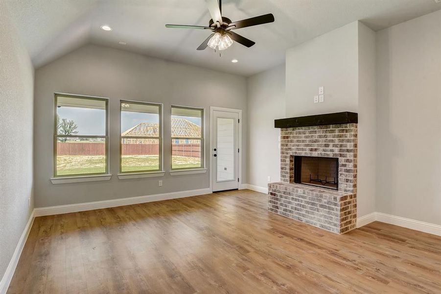 Unfurnished living room with light hardwood / wood-style floors, a brick fireplace, vaulted ceiling, and ceiling fan