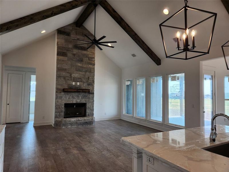 Unfurnished living room featuring high vaulted ceiling, beam ceiling, a stone fireplace, and dark hardwood / wood-style floors