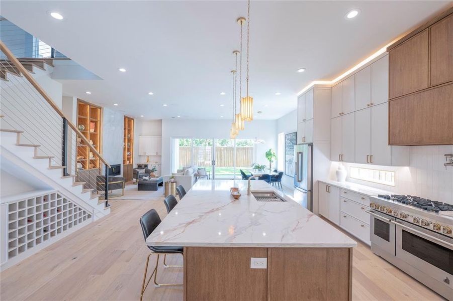 Kitchen featuring light hardwood / wood-style floors, decorative light fixtures, high end appliances, a kitchen island with sink, and white cabinetry