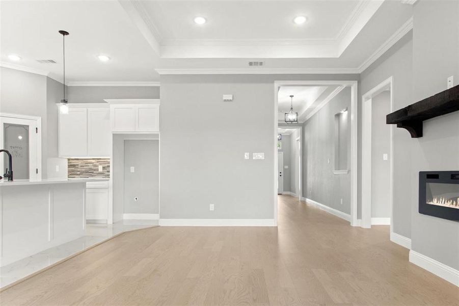 Unfurnished living room with light wood-type flooring, a tray ceiling, sink, and ornamental molding