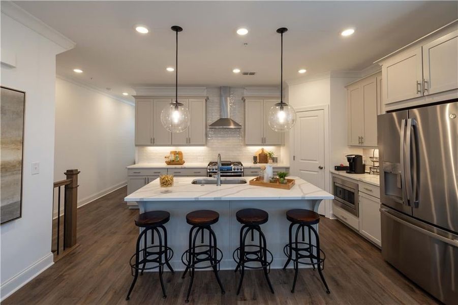 Kitchen with tasteful backsplash, wall chimney range hood, dark hardwood / wood-style floors, appliances with stainless steel finishes, and a center island with sink, refrigirator is not standard (Model Home ) not the actual unit