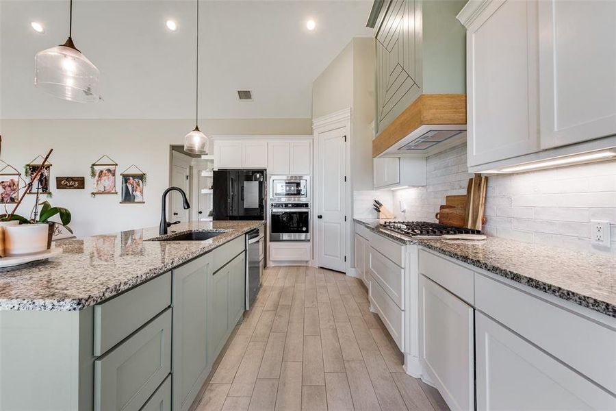 Kitchen with white cabinets, hanging light fixtures, sink, a kitchen island with sink, and appliances with stainless steel finishes