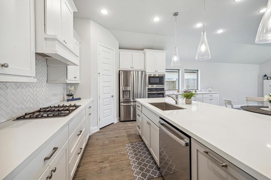 The gourmet open island kitchen area features quartz countertops, accent lighting, a tile backsplash, stainless steel appliances, and a walk-in pantry, making this a chef's dream kitchen.