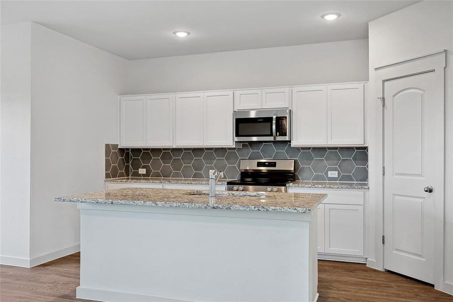 Kitchen featuring white cabinets, wood-type flooring, a kitchen island with sink, stainless steel appliances, and light stone countertops