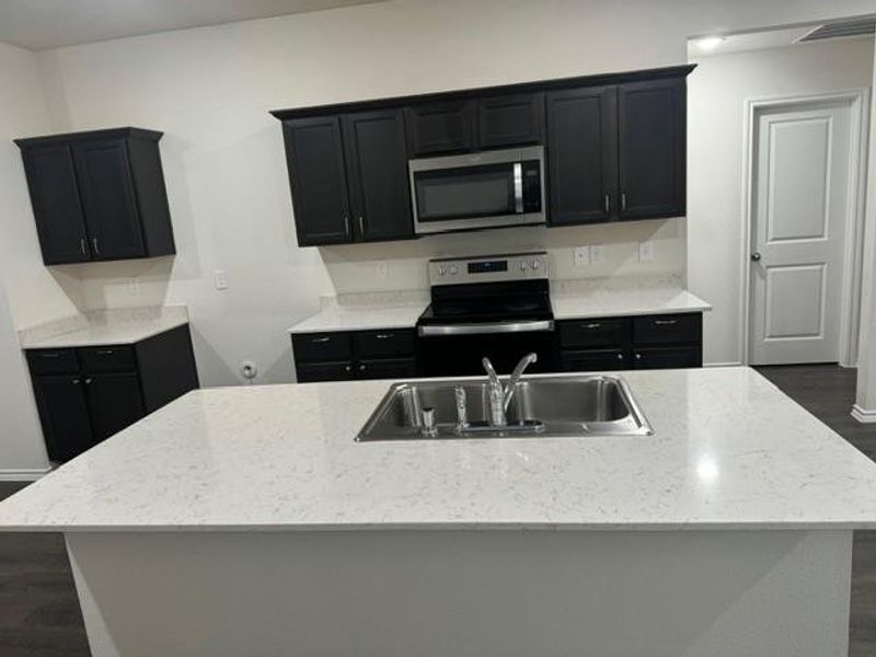 Kitchen with light stone countertops, dark hardwood / wood-style flooring, stainless steel appliances, a kitchen island with sink, and sink