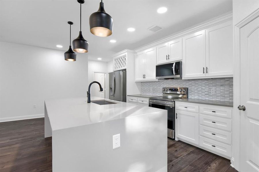 Kitchen with an island with sink, sink, appliances with stainless steel finishes, and white cabinetry