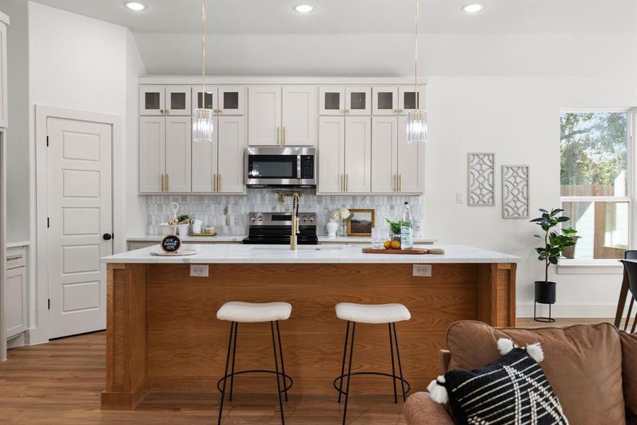 Kitchen with white cabinets, a center island with sink, appliances with stainless steel finishes, and light hardwood / wood-style floors