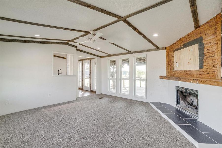 Unfurnished living room featuring dark carpet, ceiling fan, a tile fireplace, and vaulted ceiling with beams