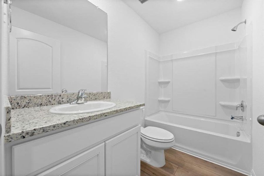 Secondary bathroom includes granite counters, designer white cabinetry and luxury vinyl plank flooring.