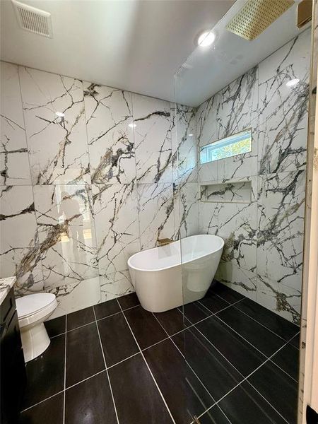 Bathroom featuring vanity, a bathtub, tile walls, and toilet