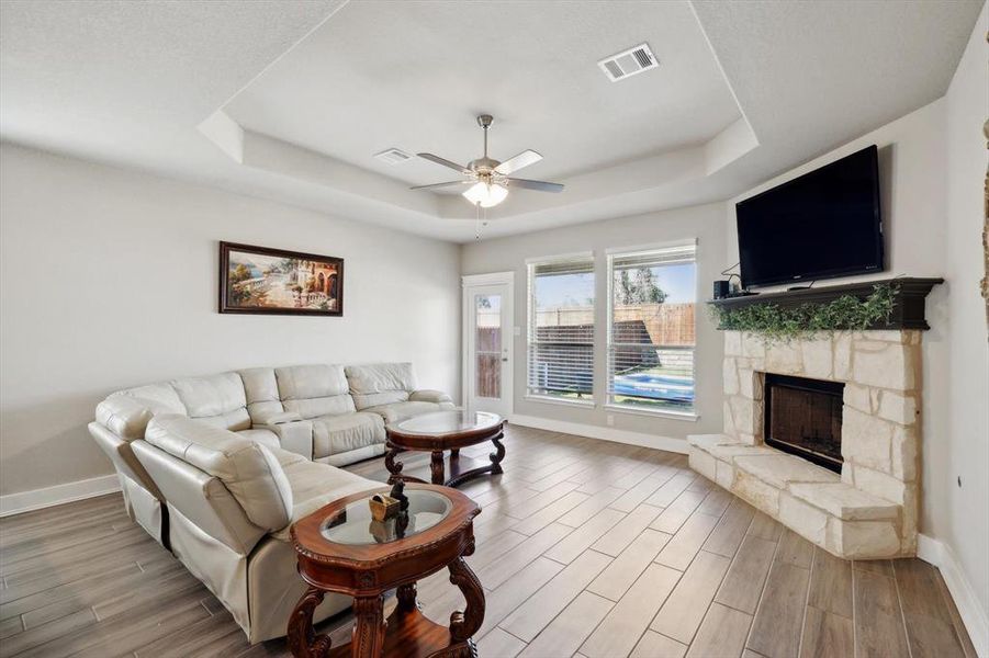 Living room with wood-type flooring, a fireplace, a tray ceiling, and ceiling fan