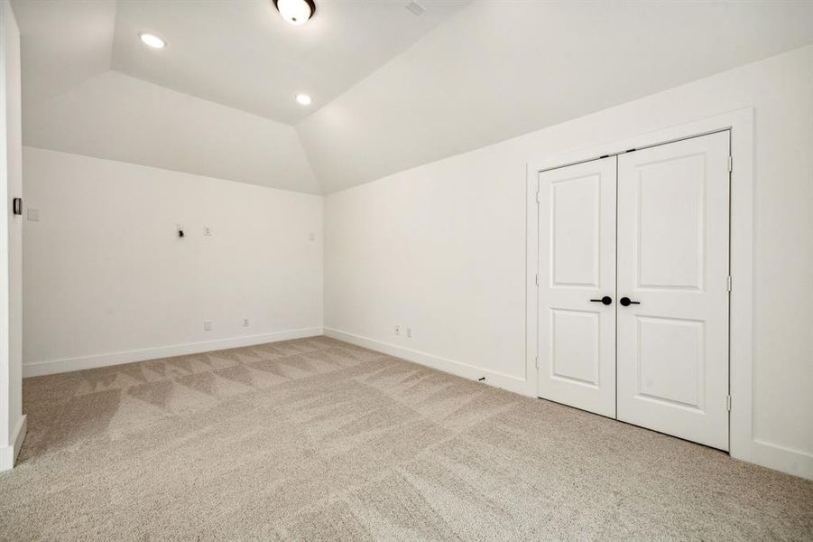 Unfurnished bedroom featuring lofted ceiling, a closet, and light colored carpet