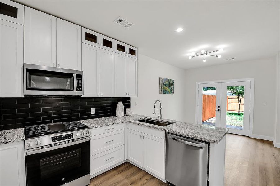 Kitchen with light wood-style floors, sink, stainless steel appliances, kitchen peninsula, and white cabinets