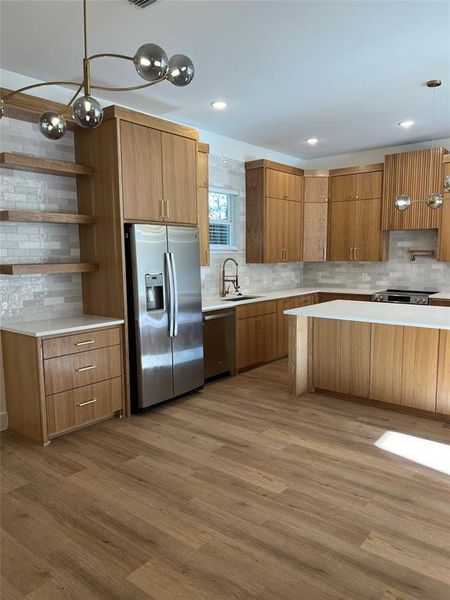 Kitchen with tasteful backsplash, light wood-type flooring, appliances with stainless steel finishes, and sink