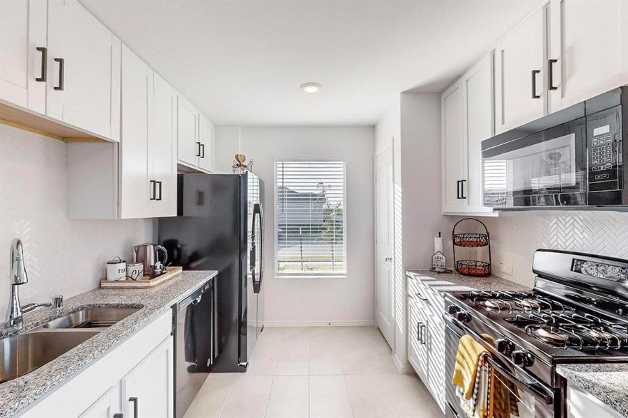 Kitchen featuring light stone counters, light tile patterned flooring, sink, white cabinetry, and black appliances